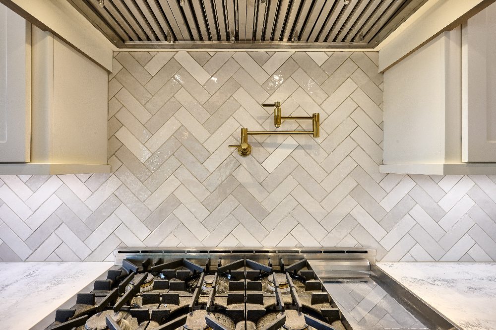 Modern kitchen with herringbone tile backsplash, gas cooktop, and brass faucet