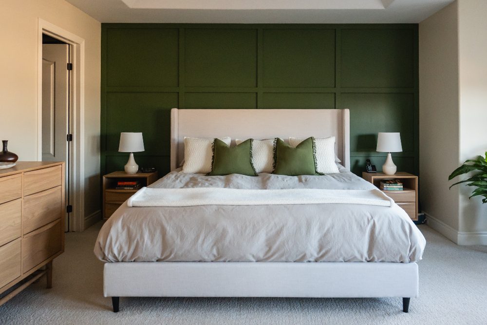 Modern bedroom with cream upholstered bed, green paneled accent wall, wooden nightstands, and neutral bedding