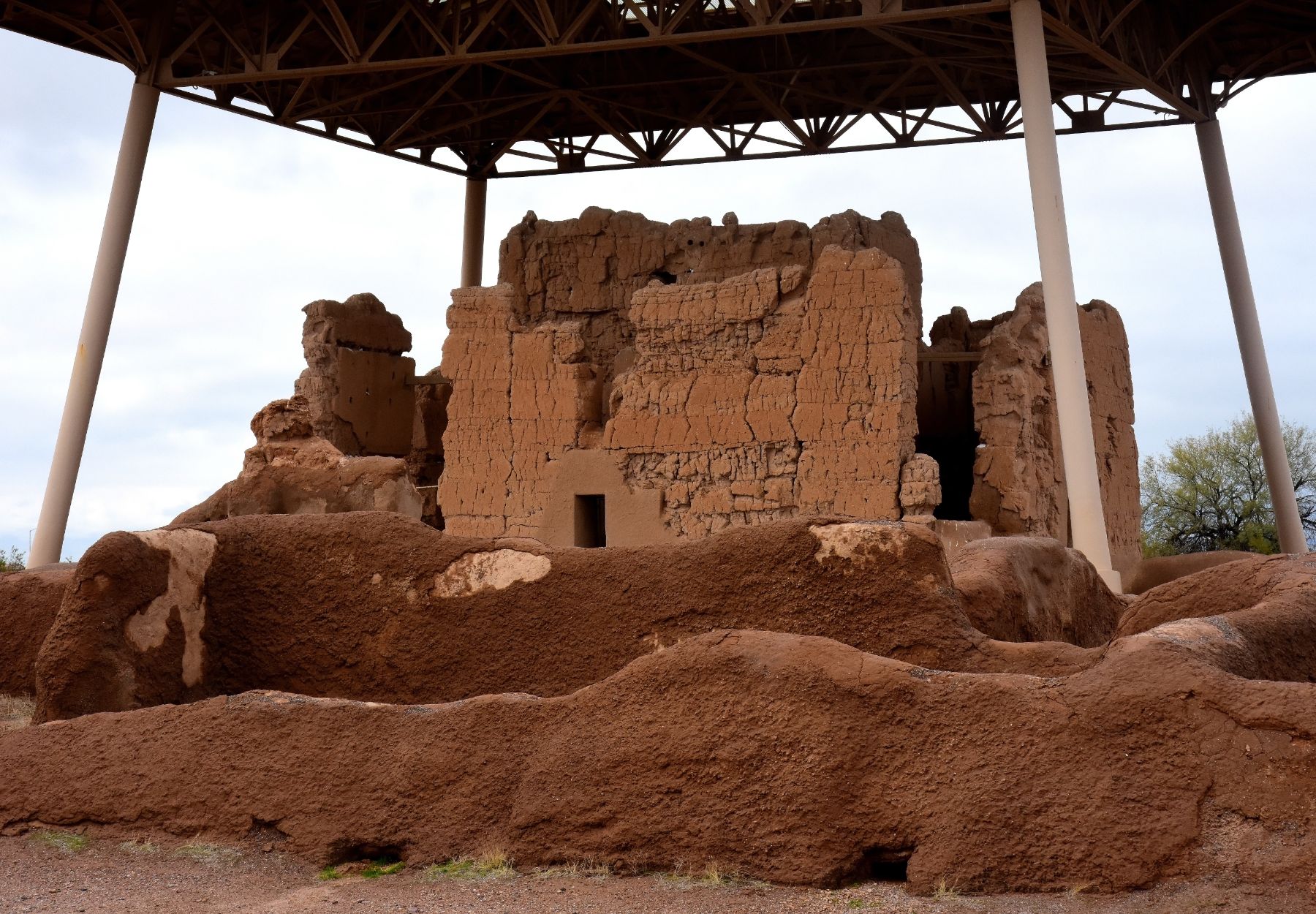 Ancient adobe ruins with protective pavilion shelter, featuring weathered brick walls and doorways