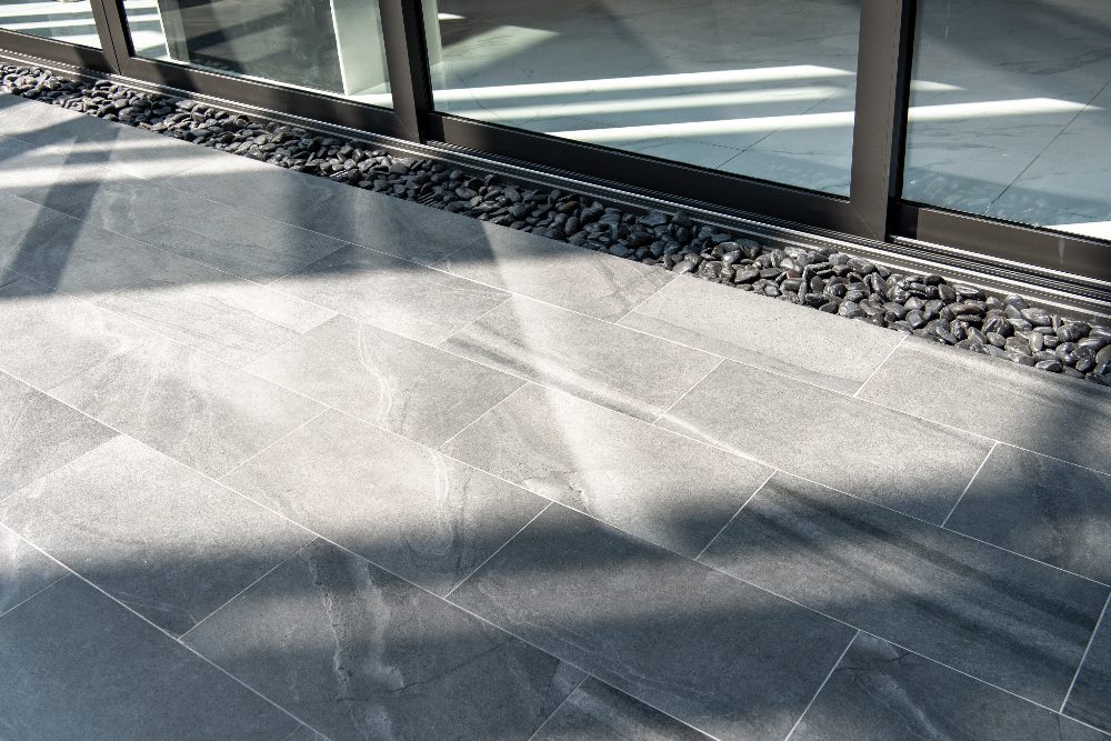 Modern patio with gray stone tiles, decorative gravel border, and glass building facade